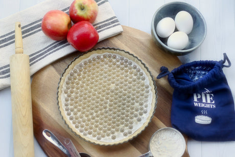 Pie crust with glass pie weights and a blue storage bag next to pie ingredients
