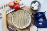 Pie crust with Gretel Baking borosilicate glass pie weights and blue storage pouch next to a pie ingredients