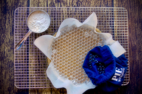 Pie crust with Gretel Baking borosilicate glass pie weights and blue storage pouch next to a cup of flour