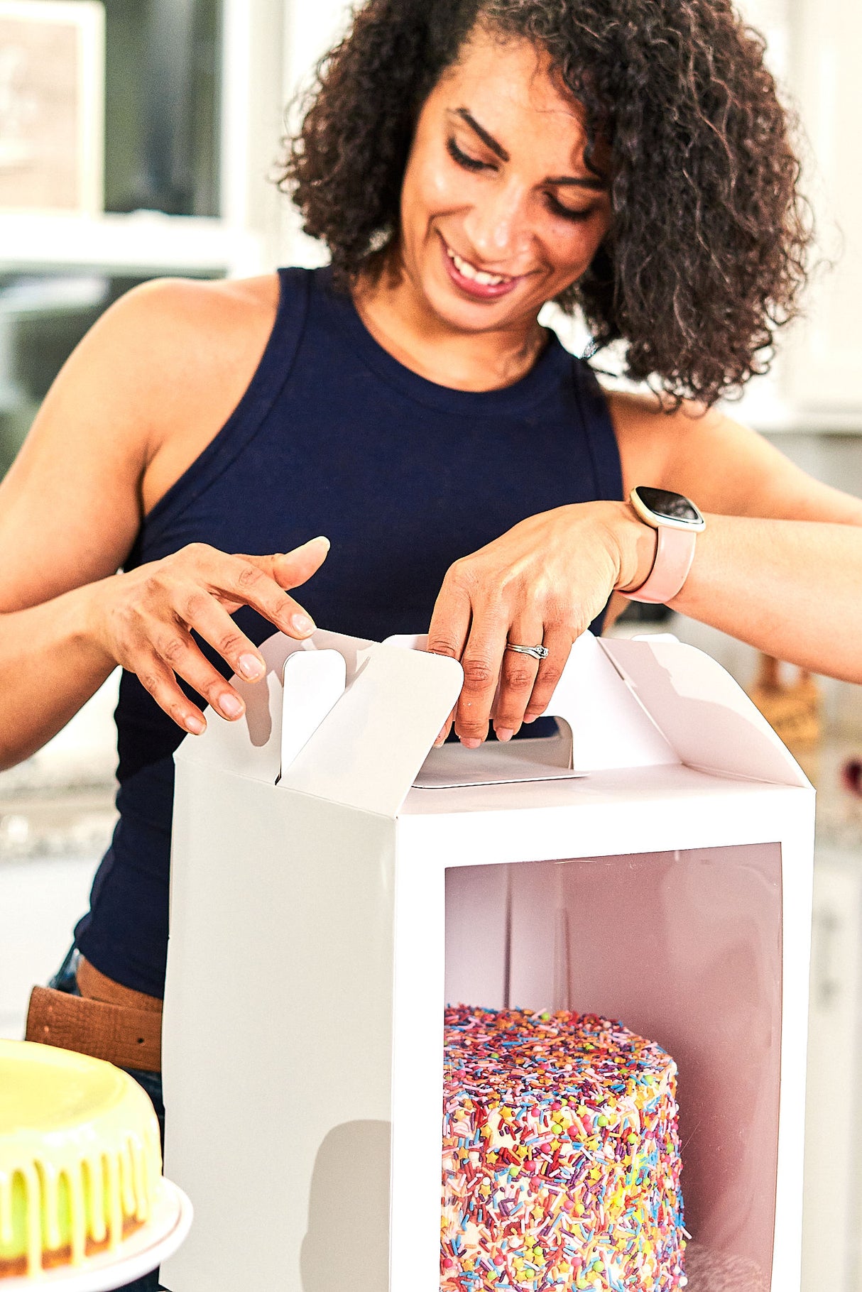 Woman closing a 10x10x12 white paper cake box with window and handle containing a cake