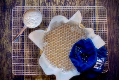 Pie crust with Gretel Baking borosilicate glass pie weights and blue storage pouch next to a cup of flour